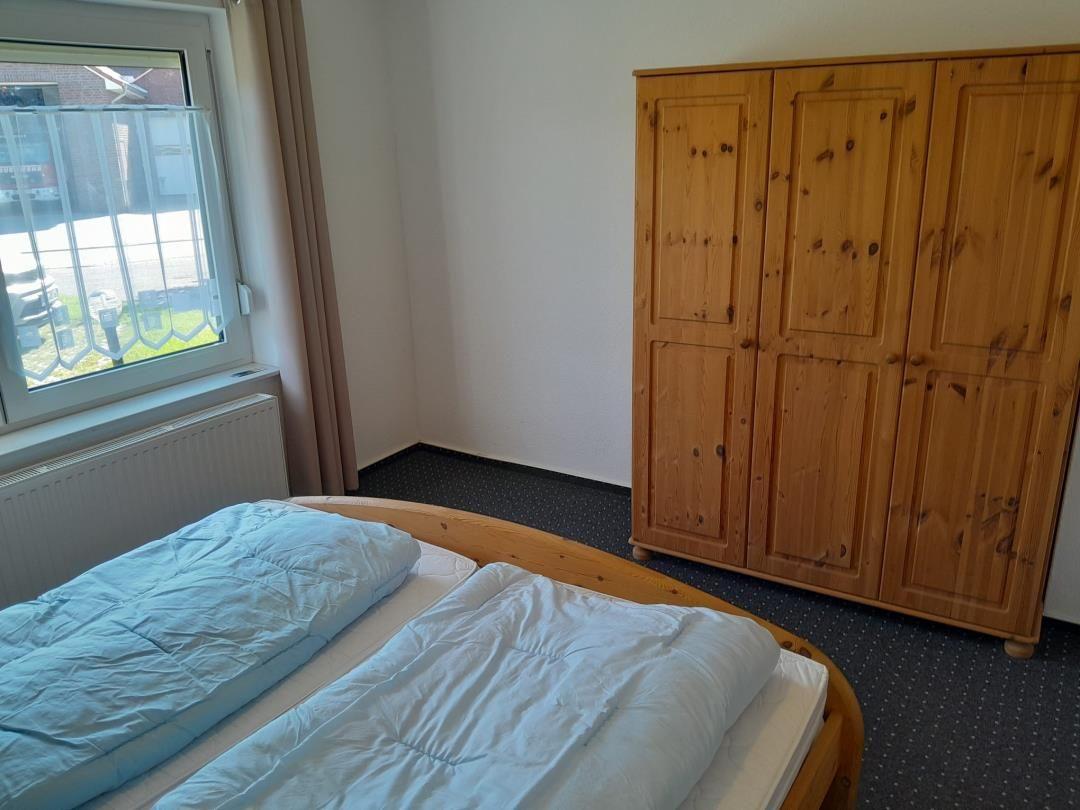 Ein Schlafzimmer mit einem Bett, einem Holzschrank und einem Fenster mit Blick nach draußen.
