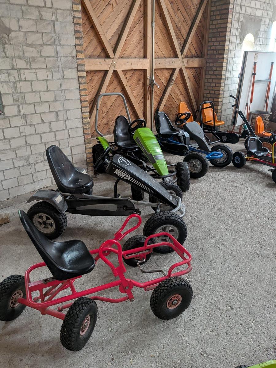 Mehrere Kinderkarts stehen in einer Garage mit Steinwand und Holztür.