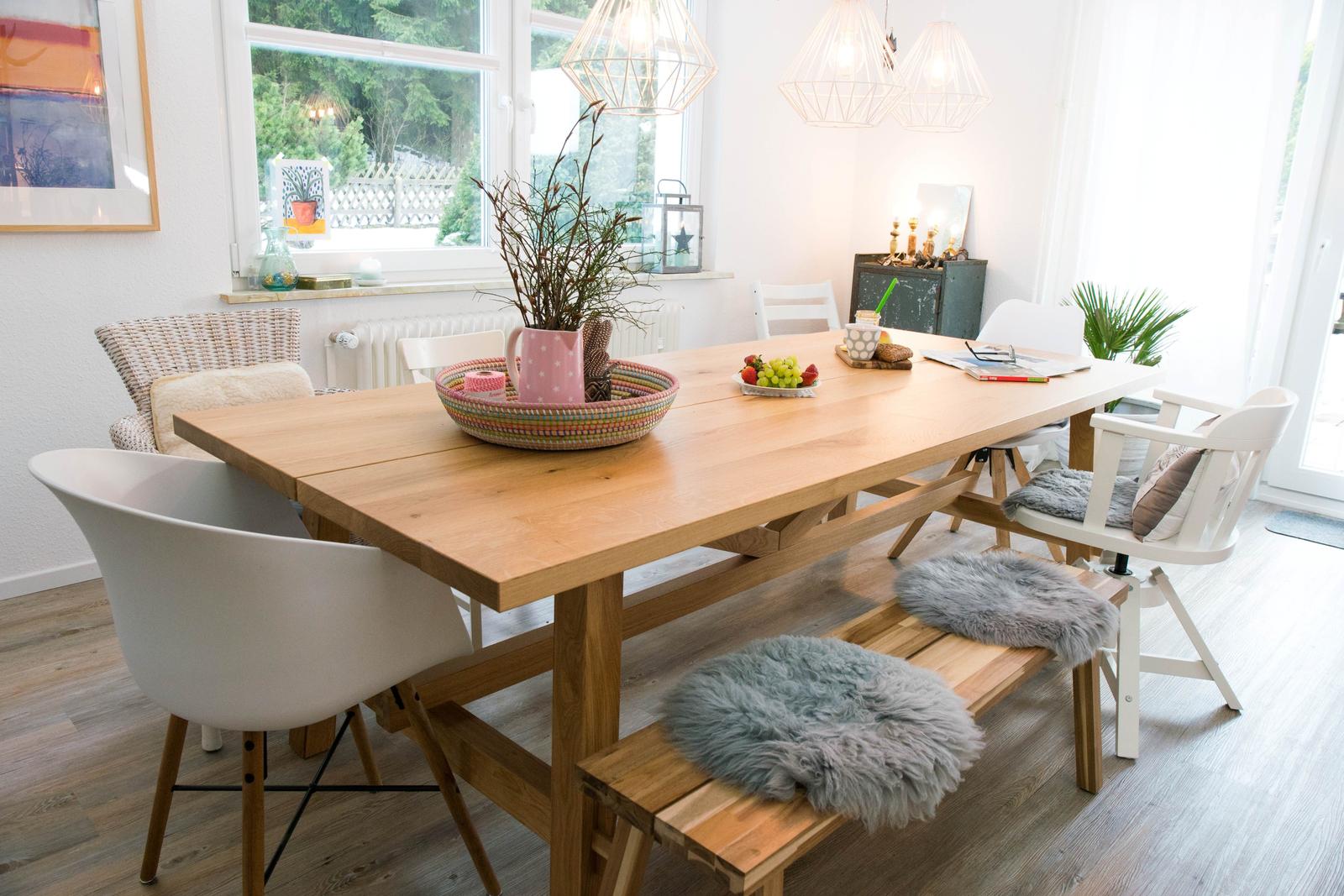 Essbereich mit Holztisch, weißen Stühlen und grauen Fellkissen.