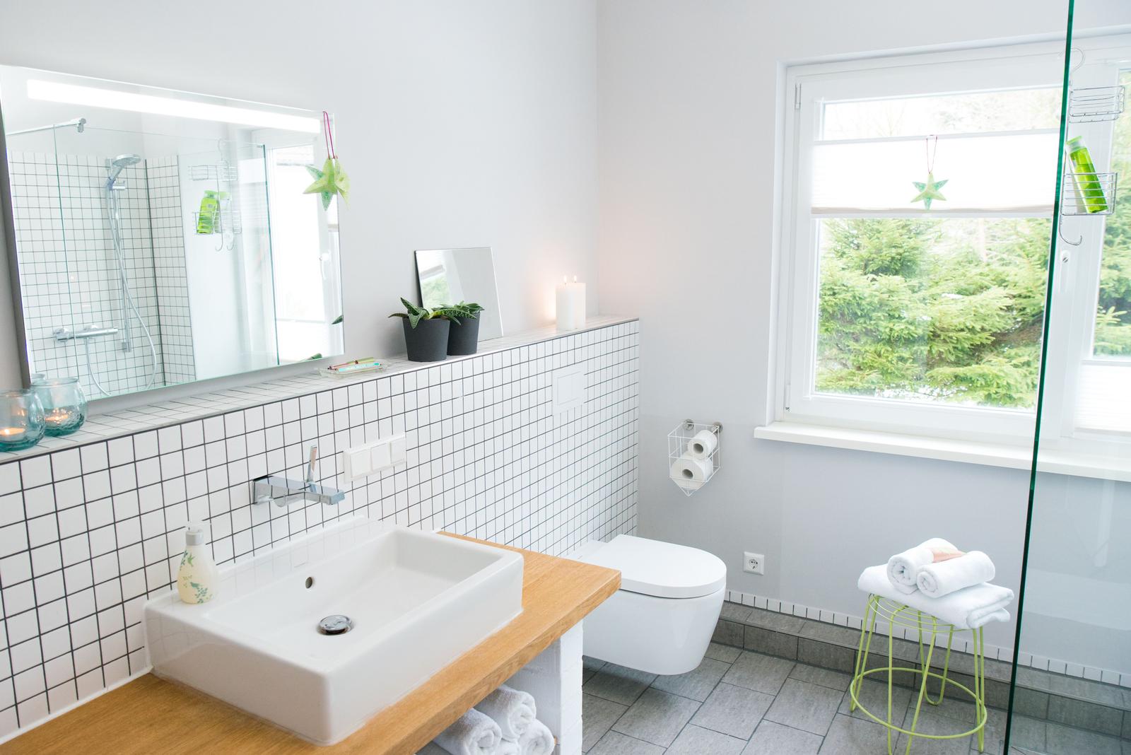 Badezimmer mit Waschbecken, Toilette und Dusche. Fenster mit Blick auf Grün.