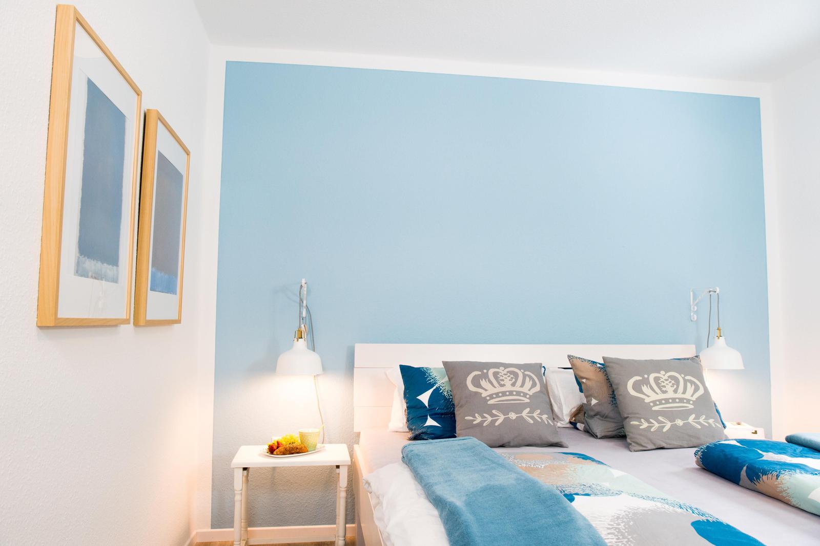 Schlafzimmer mit blauer Wand, Bett mit Kissen und Nachttisch mit Obst.