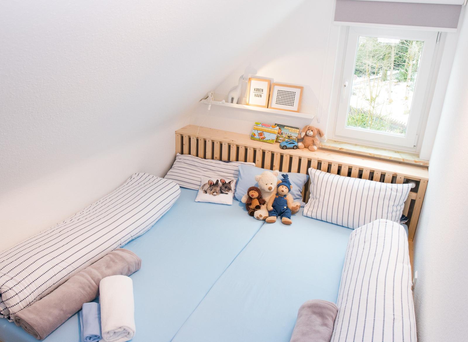 Kinderzimmer mit Bett, Kissen und Spielzeug. Fenster mit Blick auf Garten.