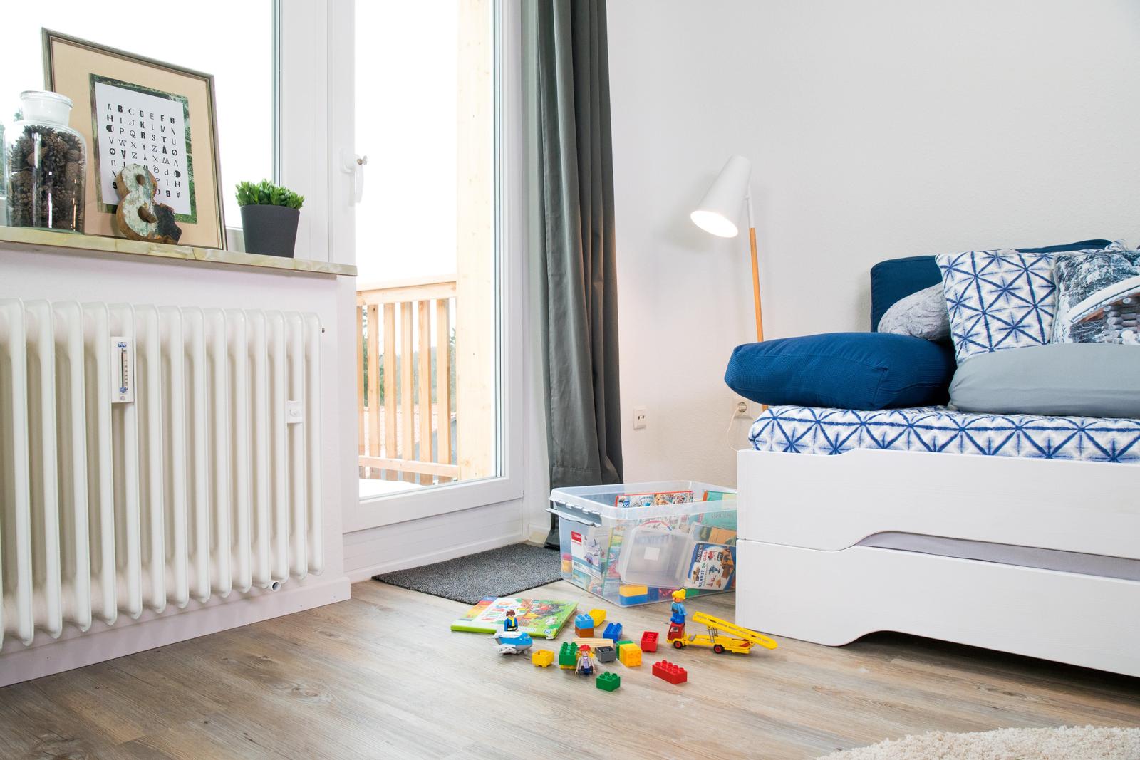 Schlafzimmer mit blauer Couch, Spielzeug und Blick auf Balkon.