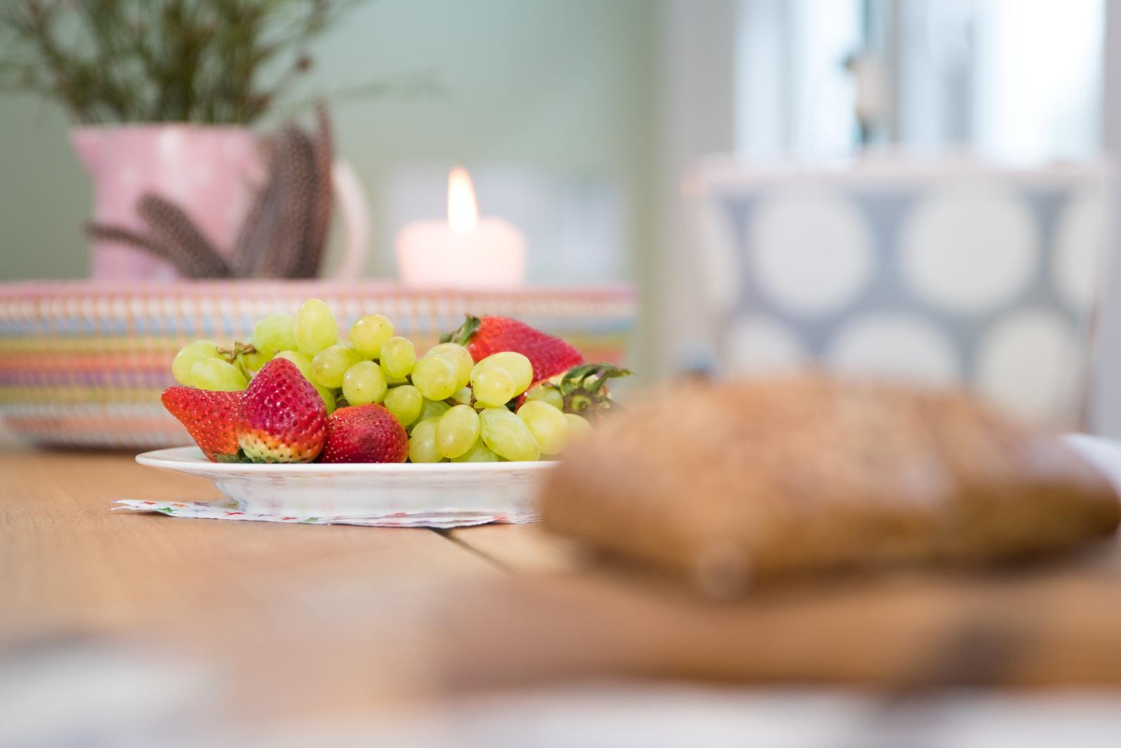 Tisch mit Obstschale, Brot und Kerze im Hintergrund.