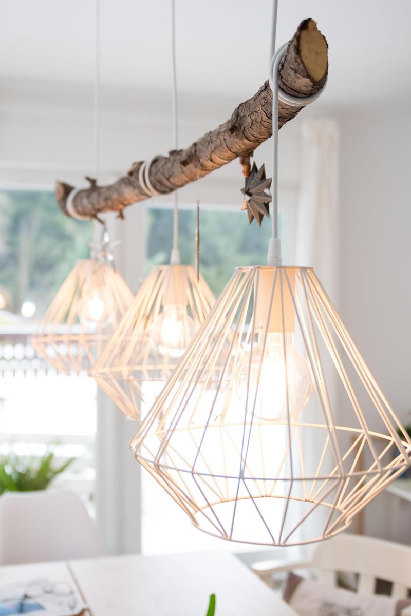 Deckenleuchte mit Holzast und geometrischen Lampenschirmen über Tisch