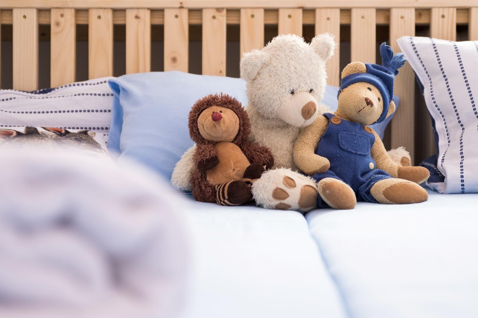 Drei Plüschtiere sitzen auf einem Bett mit Kissen und Holzgeländer.