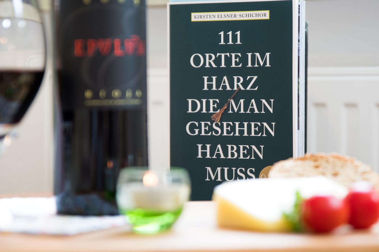 Tisch mit Buch, Wein, Käse und Tomaten. Buch: 111 Orte im Harz.