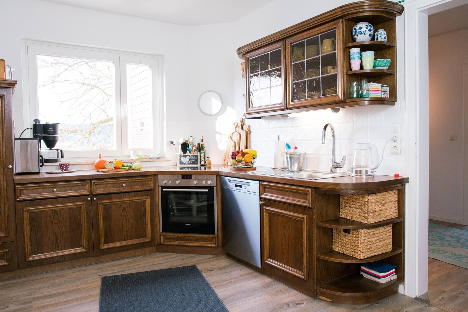 Küche mit Holzschränken, Spüle und Kochgeräten. Fenster mit Blick nach draußen.