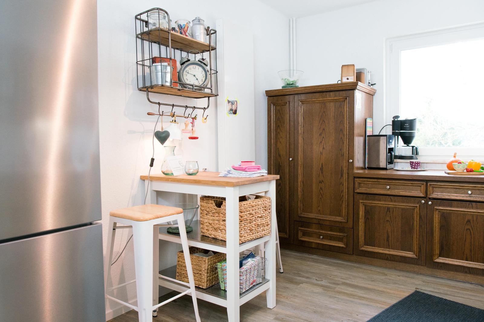Küche mit Holzschrank, Arbeitsplatte, Kühlschrank und kleinem Tisch mit Stuhl.