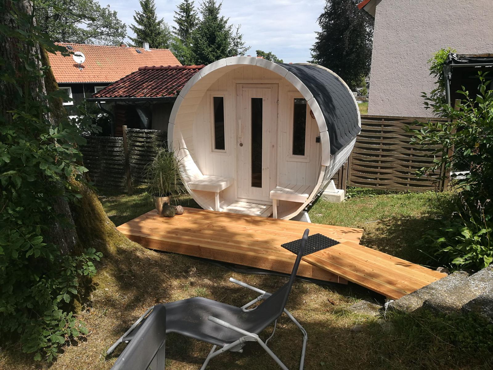 Rundes Holzbad mit Dach, Terrasse und Stuhl im Garten.