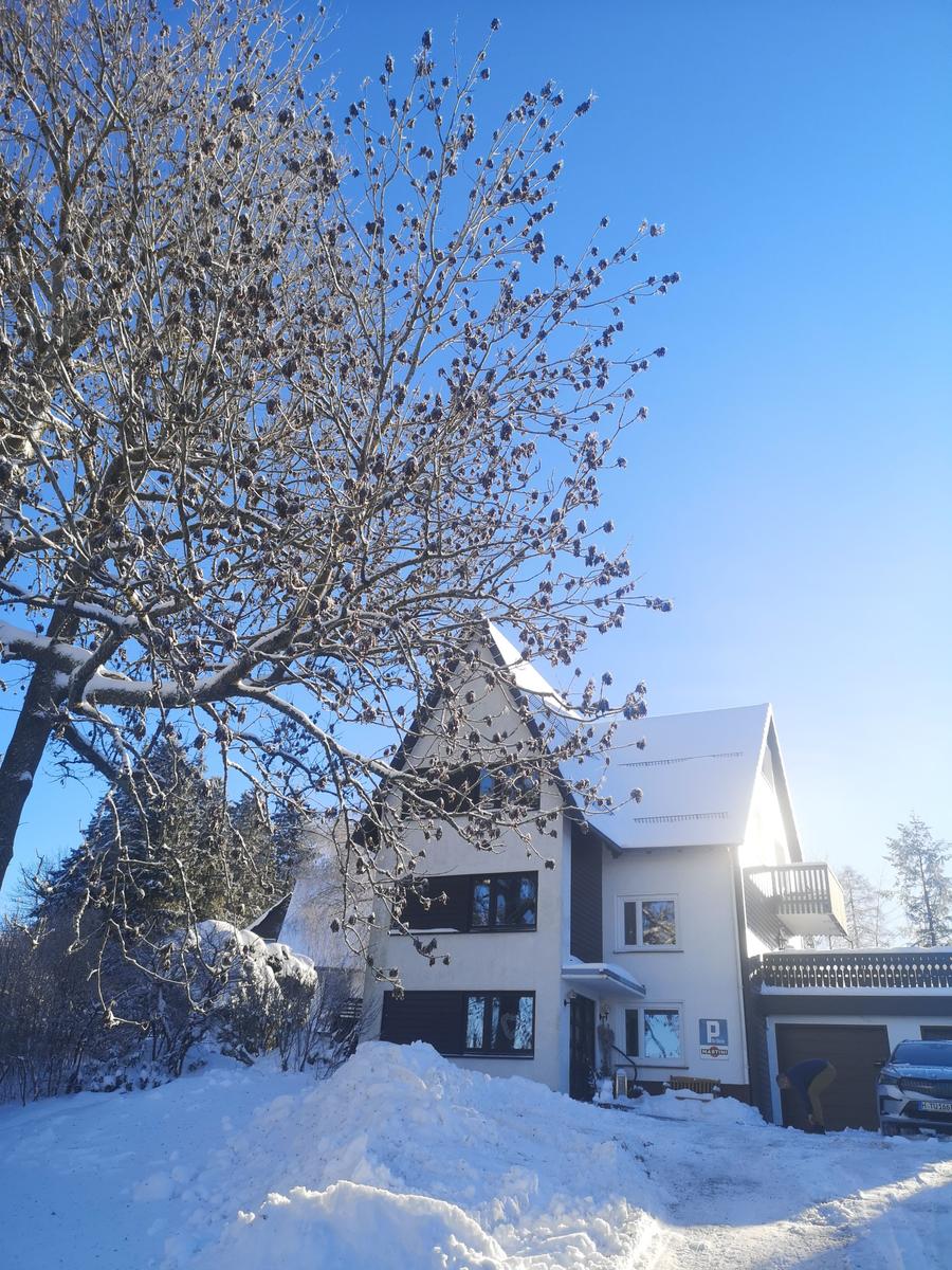 Schneebedecktes Haus mit Balkon und Garage unter blauem Himmel.