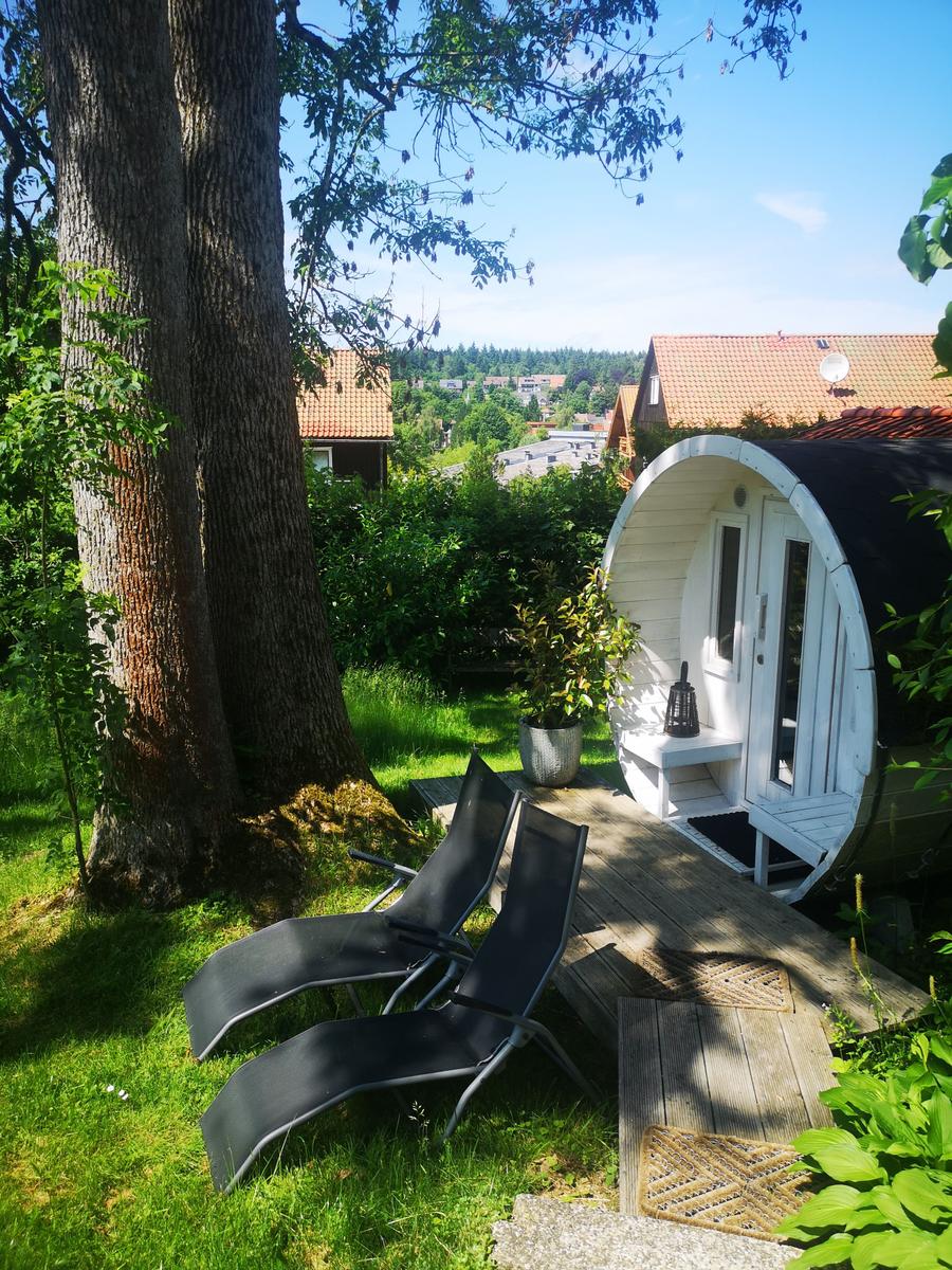 Rundes Holzhaus mit Terrasse, Sonnenliegen und Blick auf Wohnhäuser.