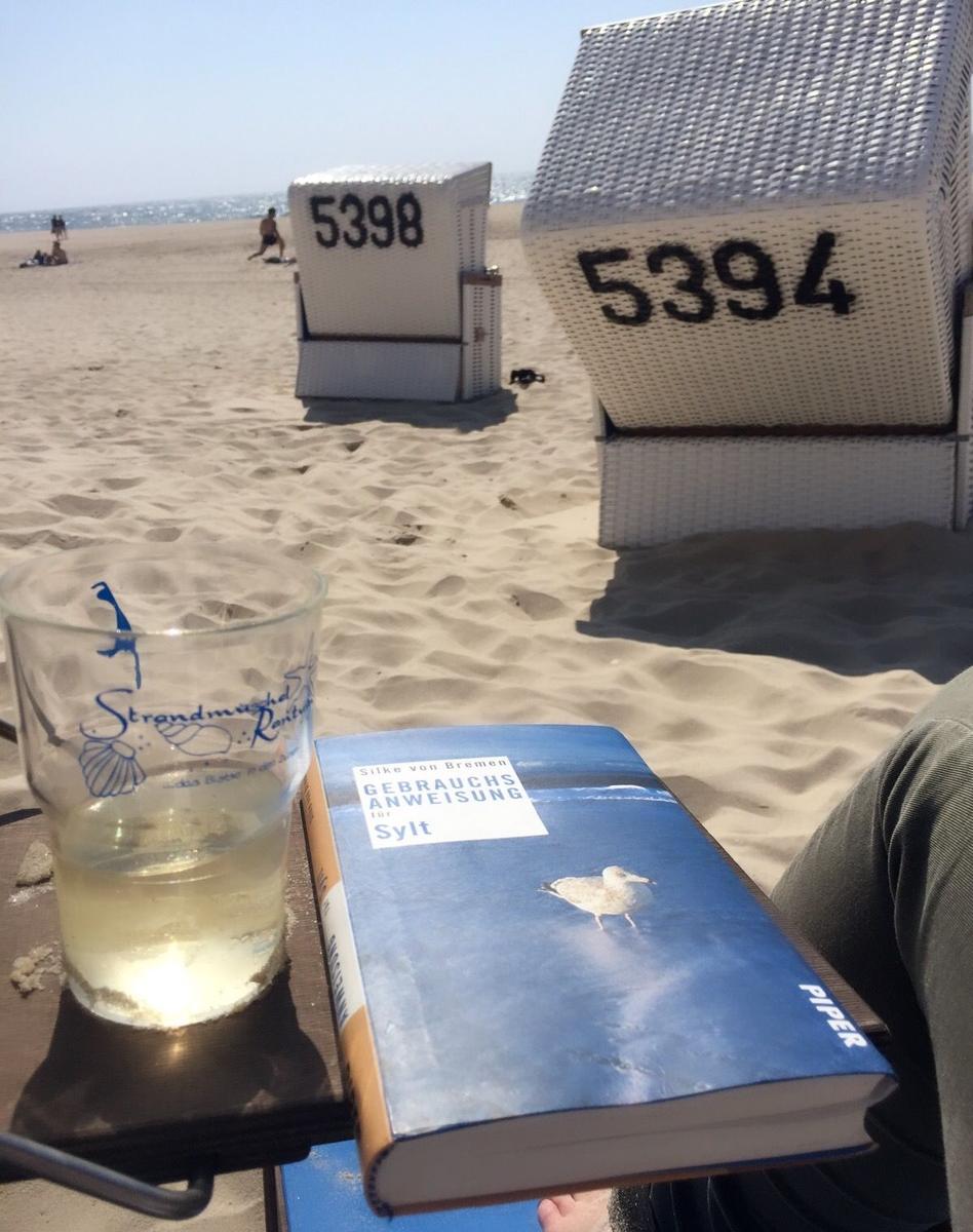 Strandkörbe mit Nummern, Buch und Getränk auf dem Sand.
