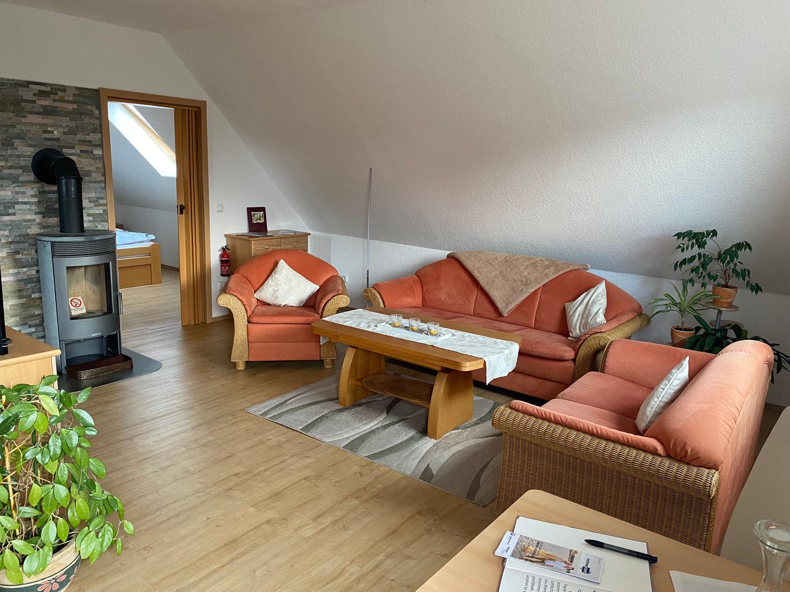 Wohnzimmer mit orangefarbenen Sitzmöbeln, Holztisch und Kaminofen.