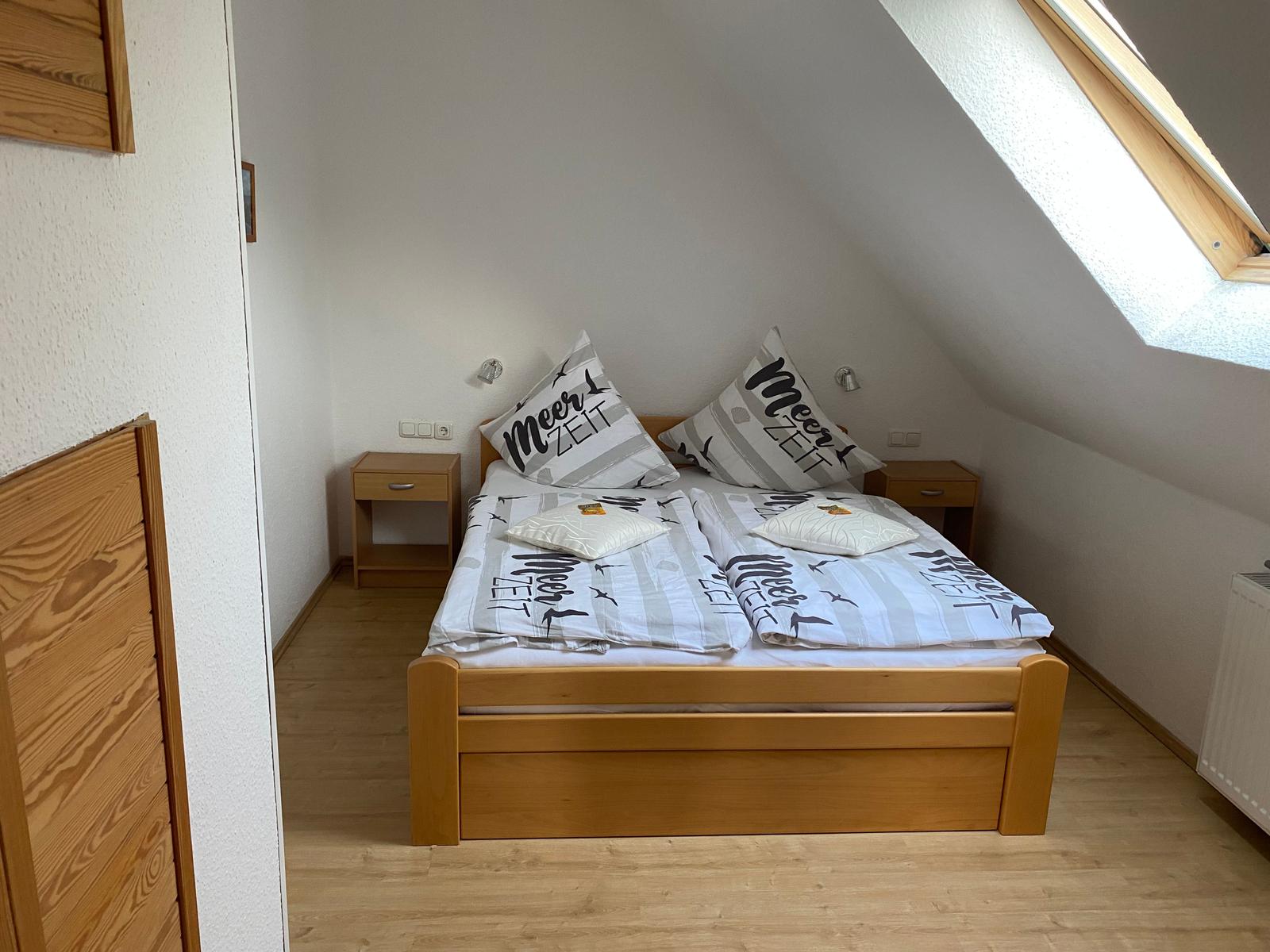 Doppelbett mit Bettwäsche, zwei Nachttische und Dachschräge mit Fenster.