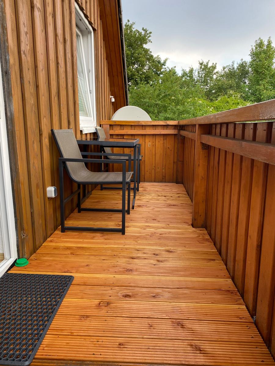 Holzterrasse mit Sitzgelegenheit und Blick auf Bäume.