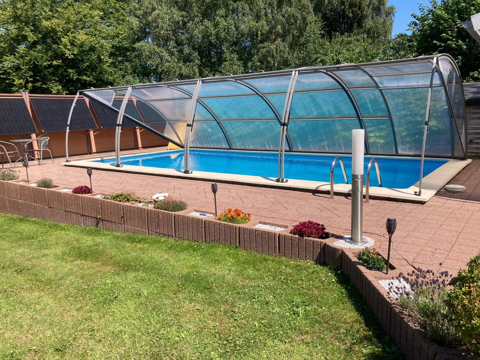 Pool mit Glasabdeckung, umgeben von gepflastertem Bereich und Grünfläche.