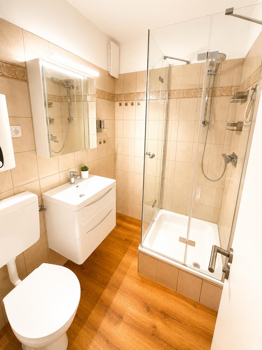 Badezimmer mit Dusche, Waschbecken und Toilette auf Holzfußboden.