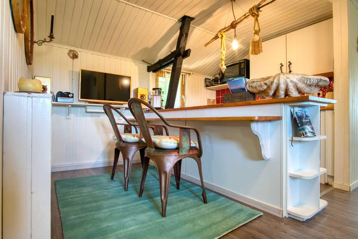 Ein Raum mit Kücheninsel, zwei Stühlen und Fernseher an der Wand.