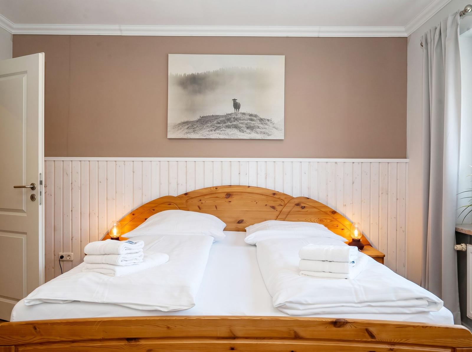Doppelbett mit weißer Bettwäsche, Holzgestell und Wandbild mit Schaf.