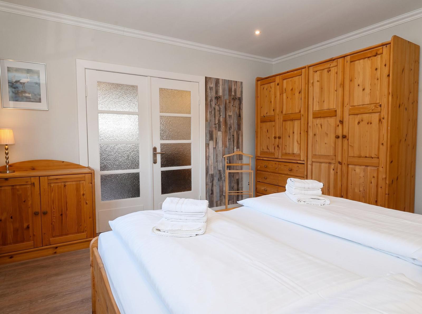 Schlafzimmer mit Holzbett, Kleiderschrank und Tür mit getöntem Glas.