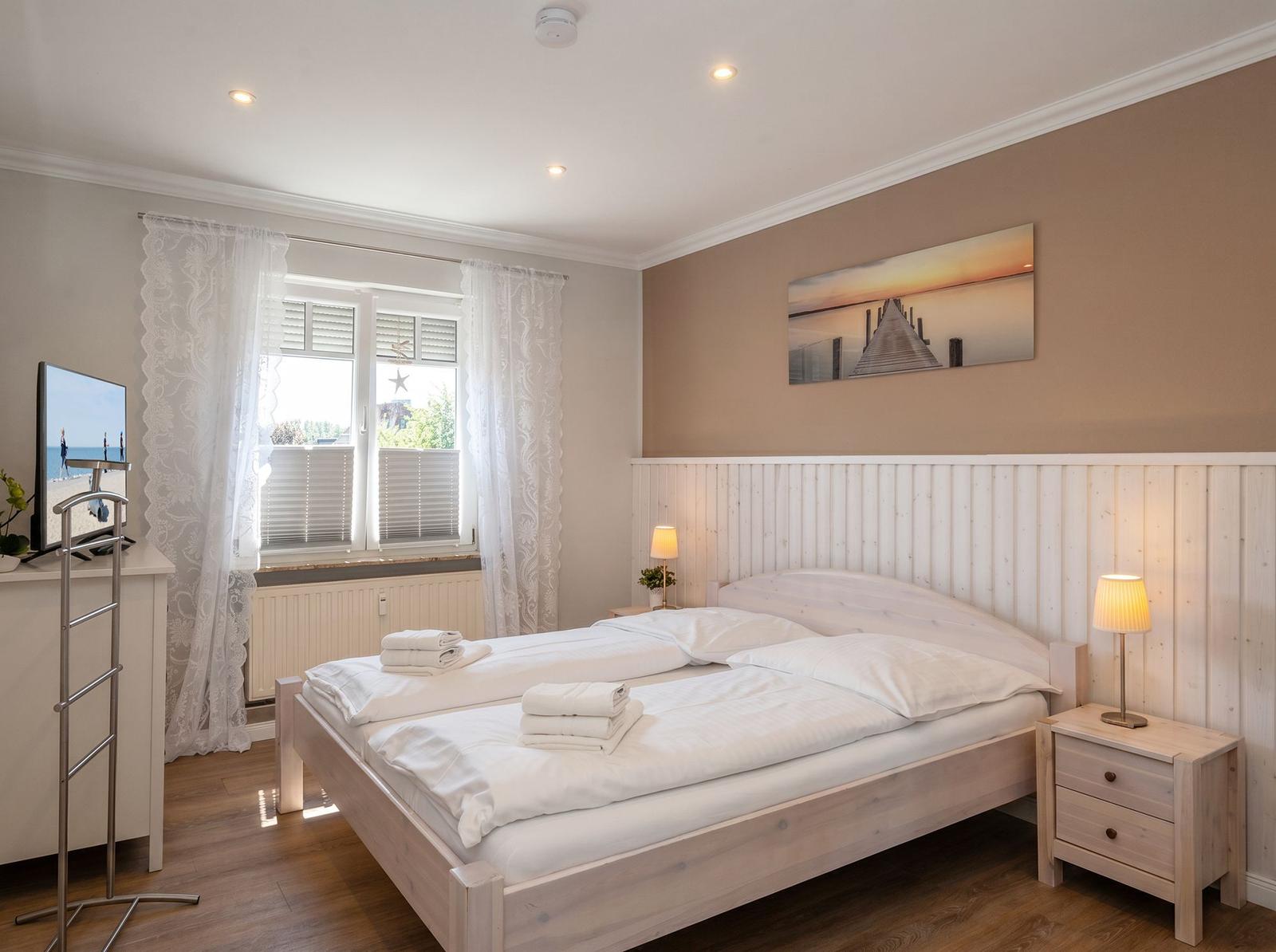 Schlafzimmer mit Doppelbett, Fenster, Nachttisch und Wandbild.