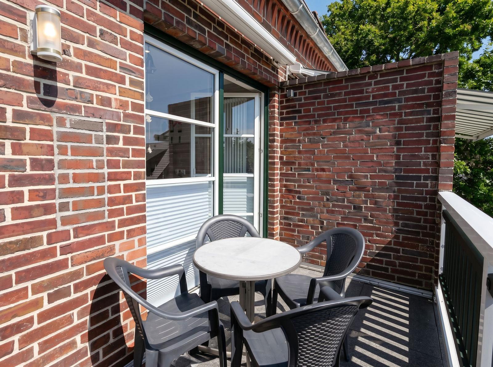 Terrasse mit Tisch und vier Stühlen, umgeben von Backsteinmauern und einer Glastür.