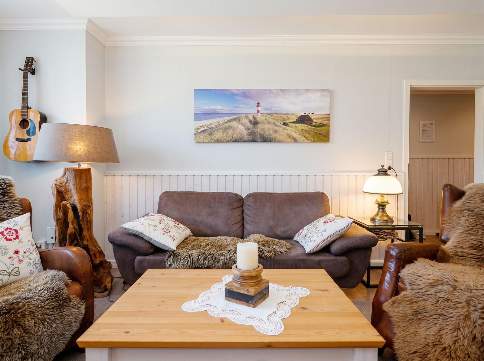 Wohnzimmer mit Sofa, zwei Sesseln, Couchtisch und Wandbild mit Leuchtturm.