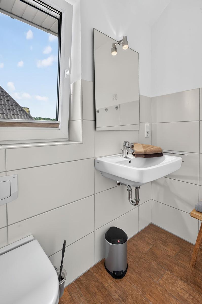 Badezimmer mit Waschbecken, Spiegel, Fenster und Toilette.