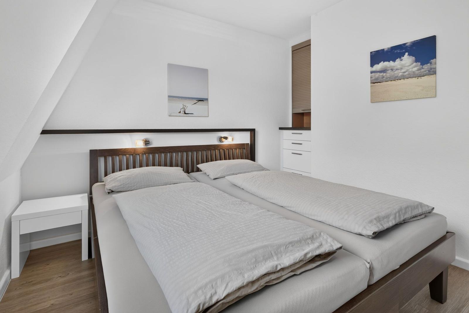 Schlafzimmer mit Doppelbett, Nachttisch und Wandbildern.