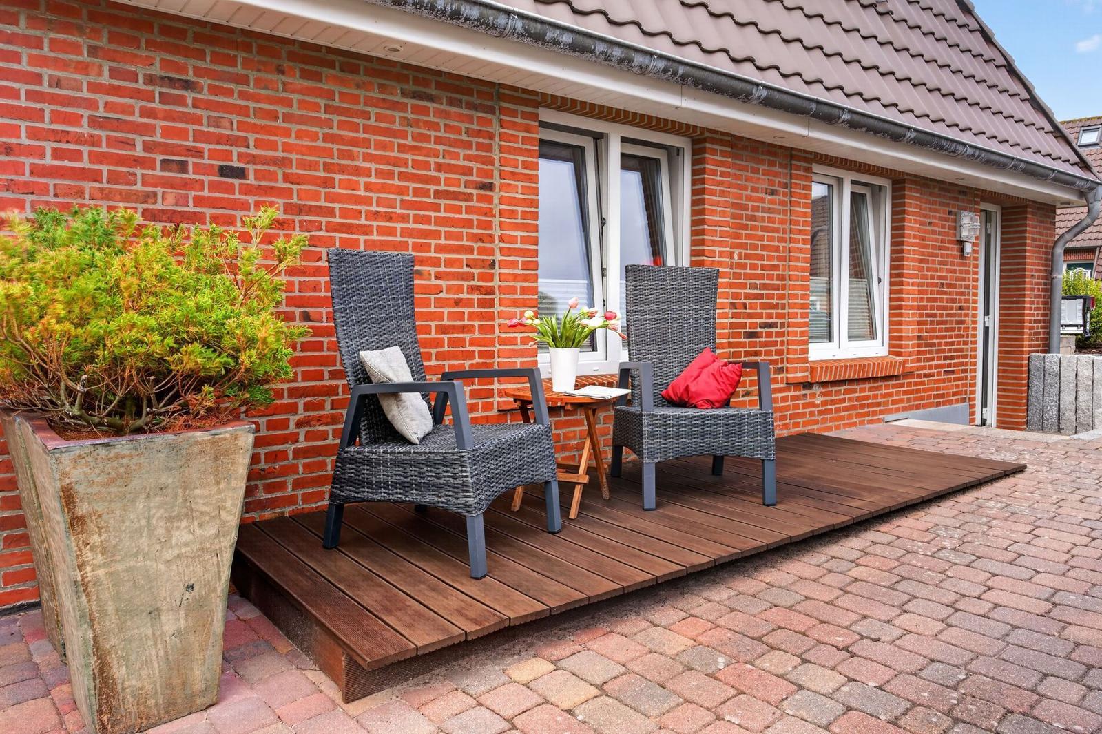 Terrasse mit zwei Stühlen, Tisch und Pflanze vor Backsteinhaus.