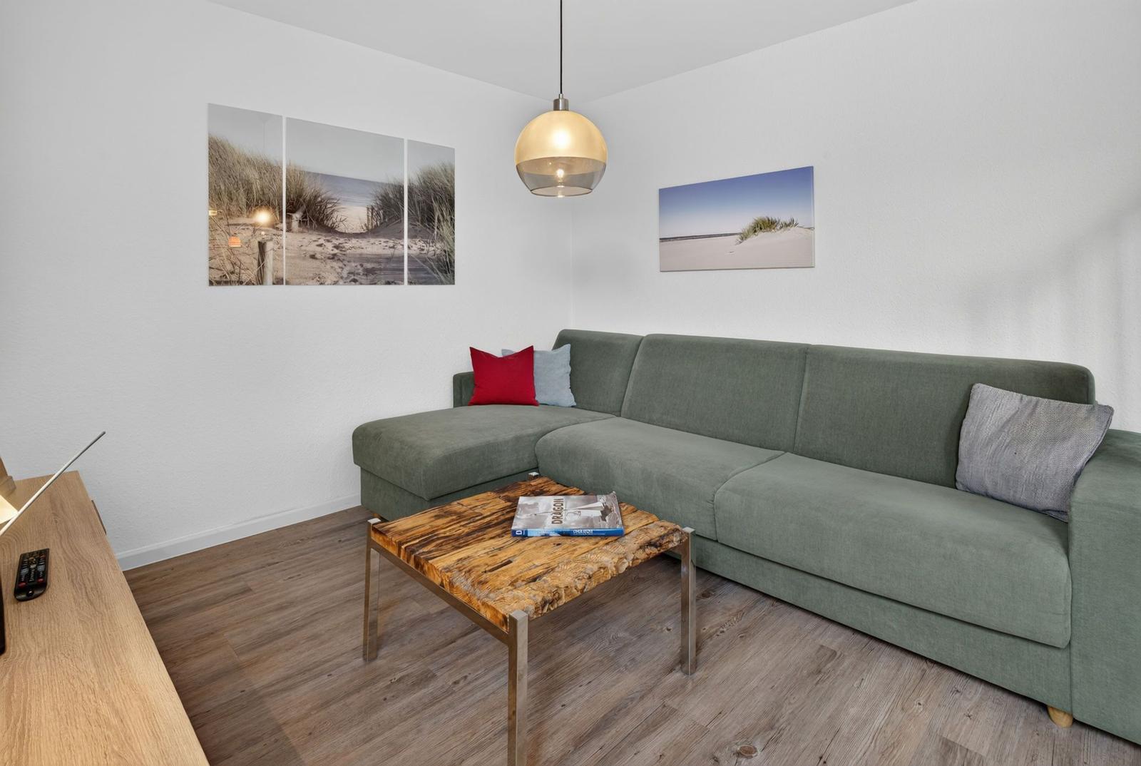 Ein Wohnzimmer mit grünem Sofa, Holztisch und Wandbildern.