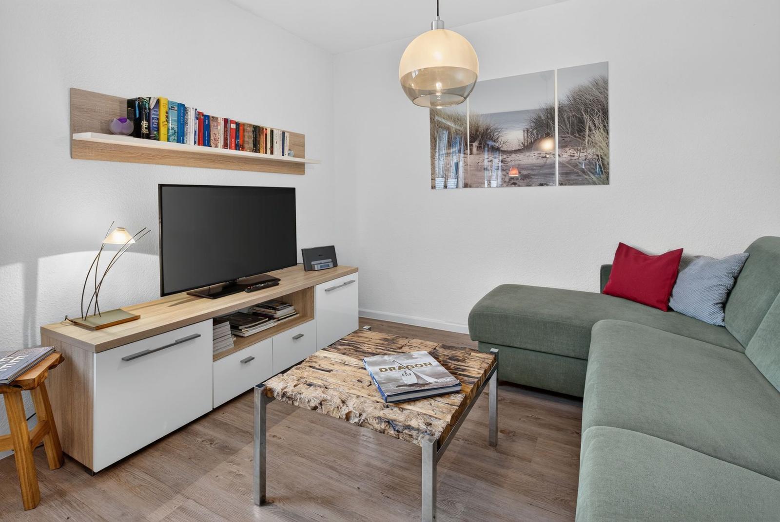 Ein Wohnzimmer mit grünem Sofa, Holzfußboden und Fernseher auf einem Holzregal.