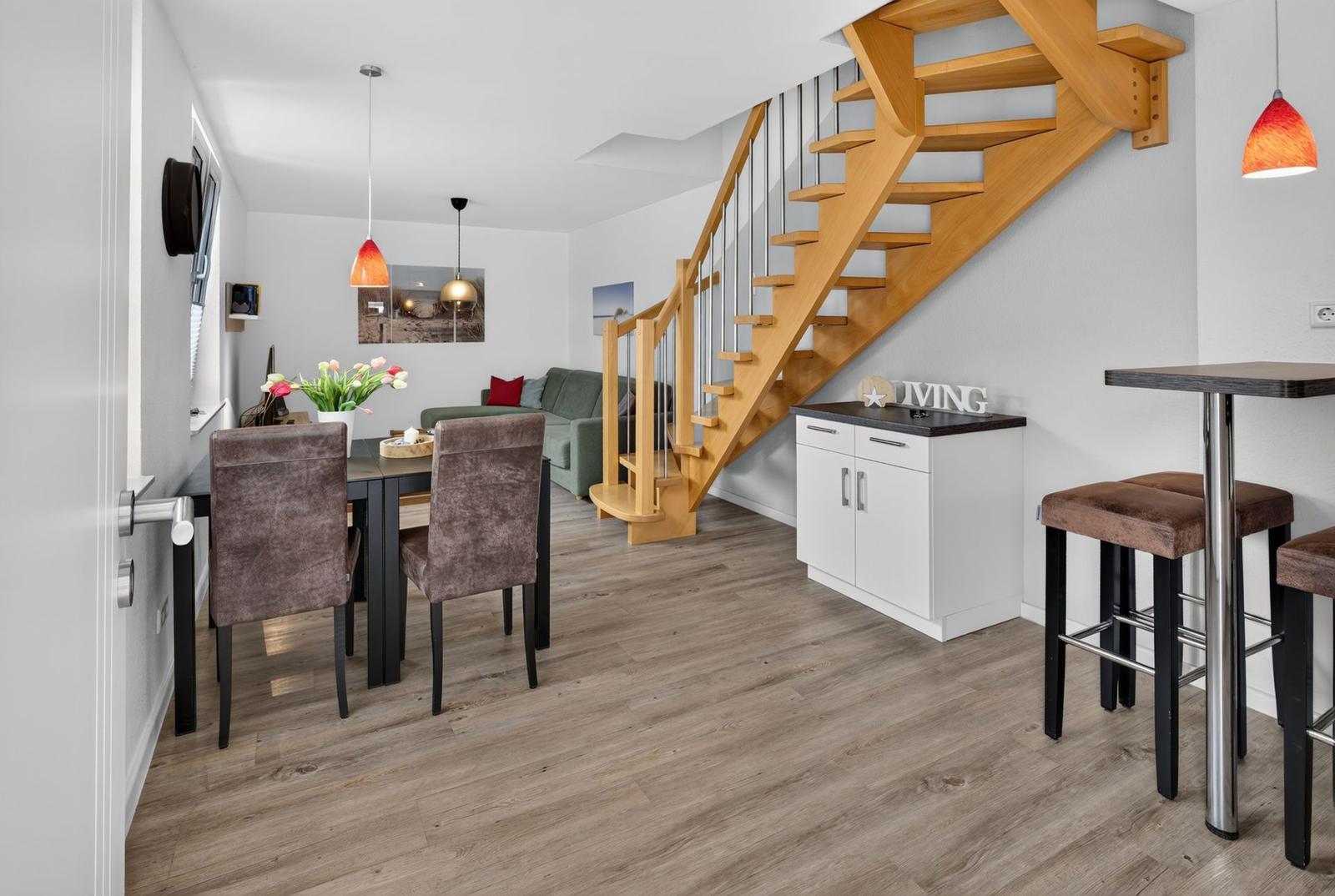 Eingangsbereich mit Essbereich, Treppenhaus und Barhocker. Holzfußboden und helle Wände.