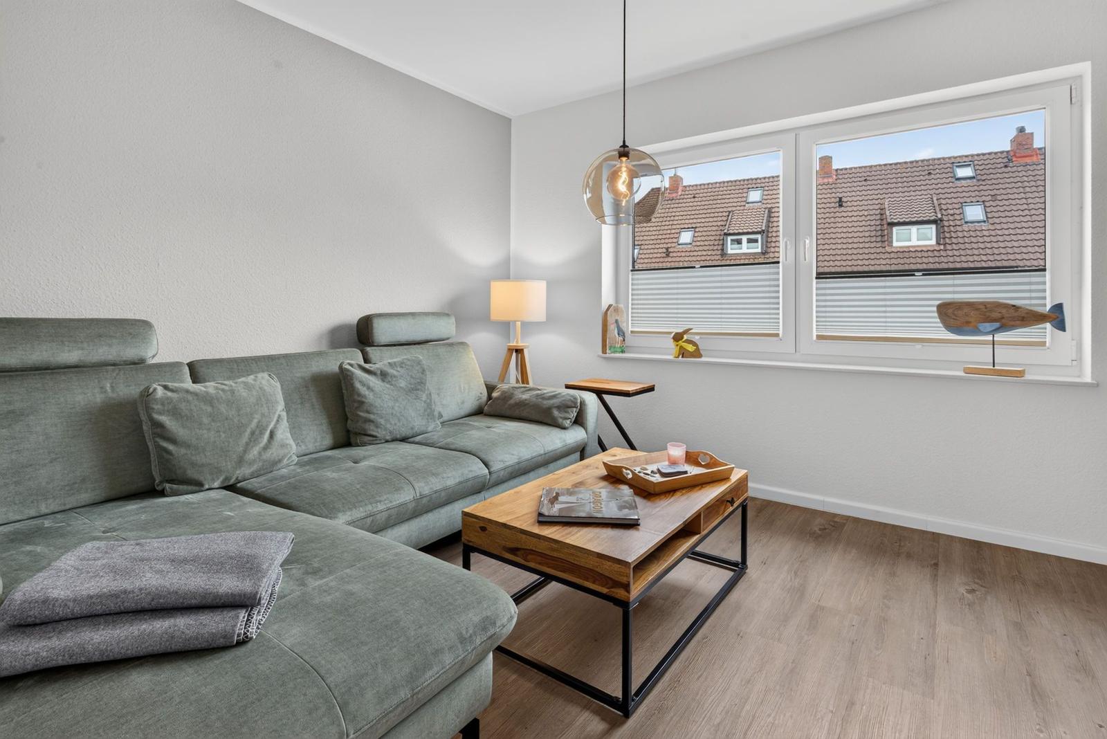 Wohnzimmer mit Sofa, Couchtisch und Fenster mit Blick auf Dächer.