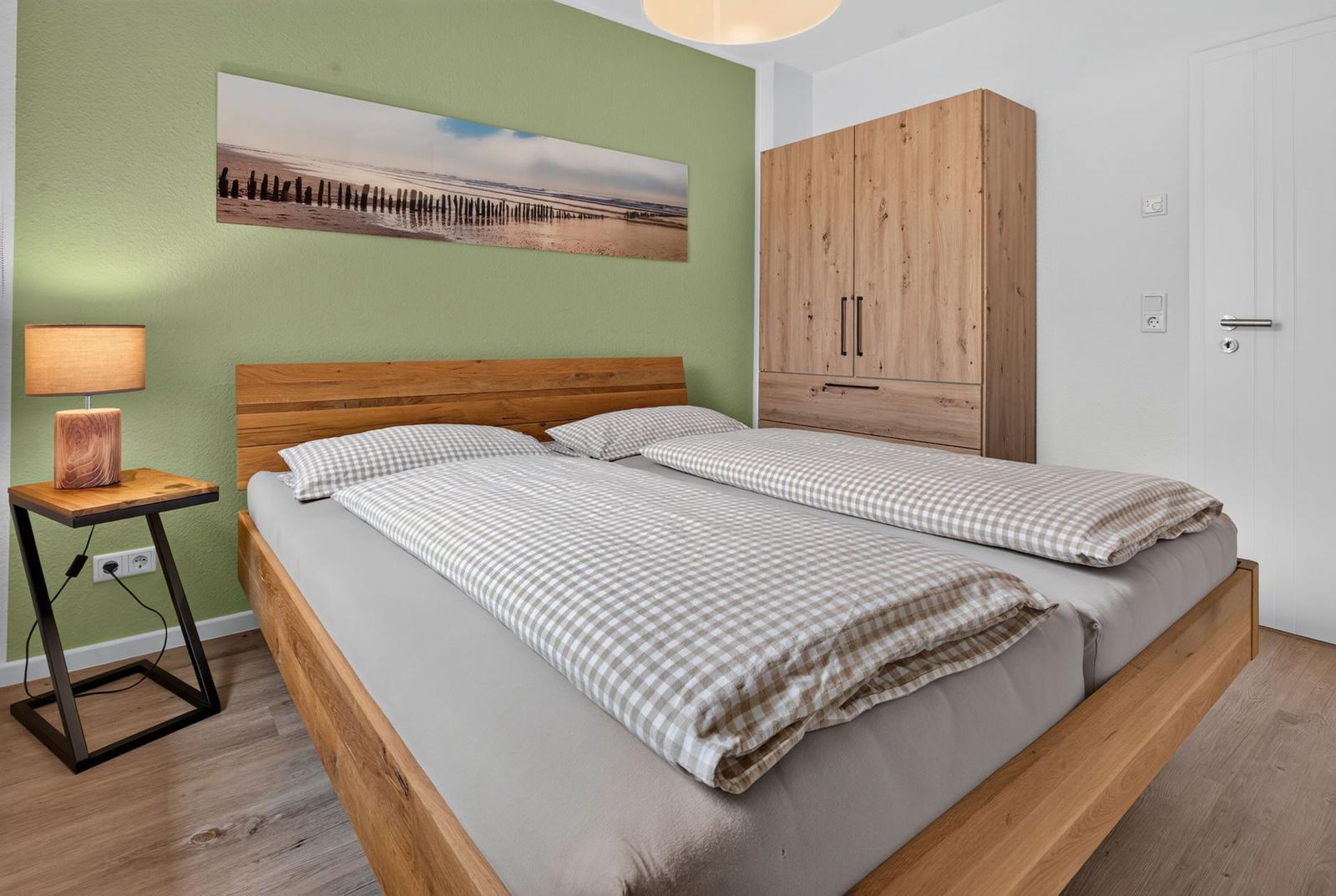 Schlafzimmer mit Doppelbett, Holzmöbel und Wandbild. Holzfußboden und grüne Wand.