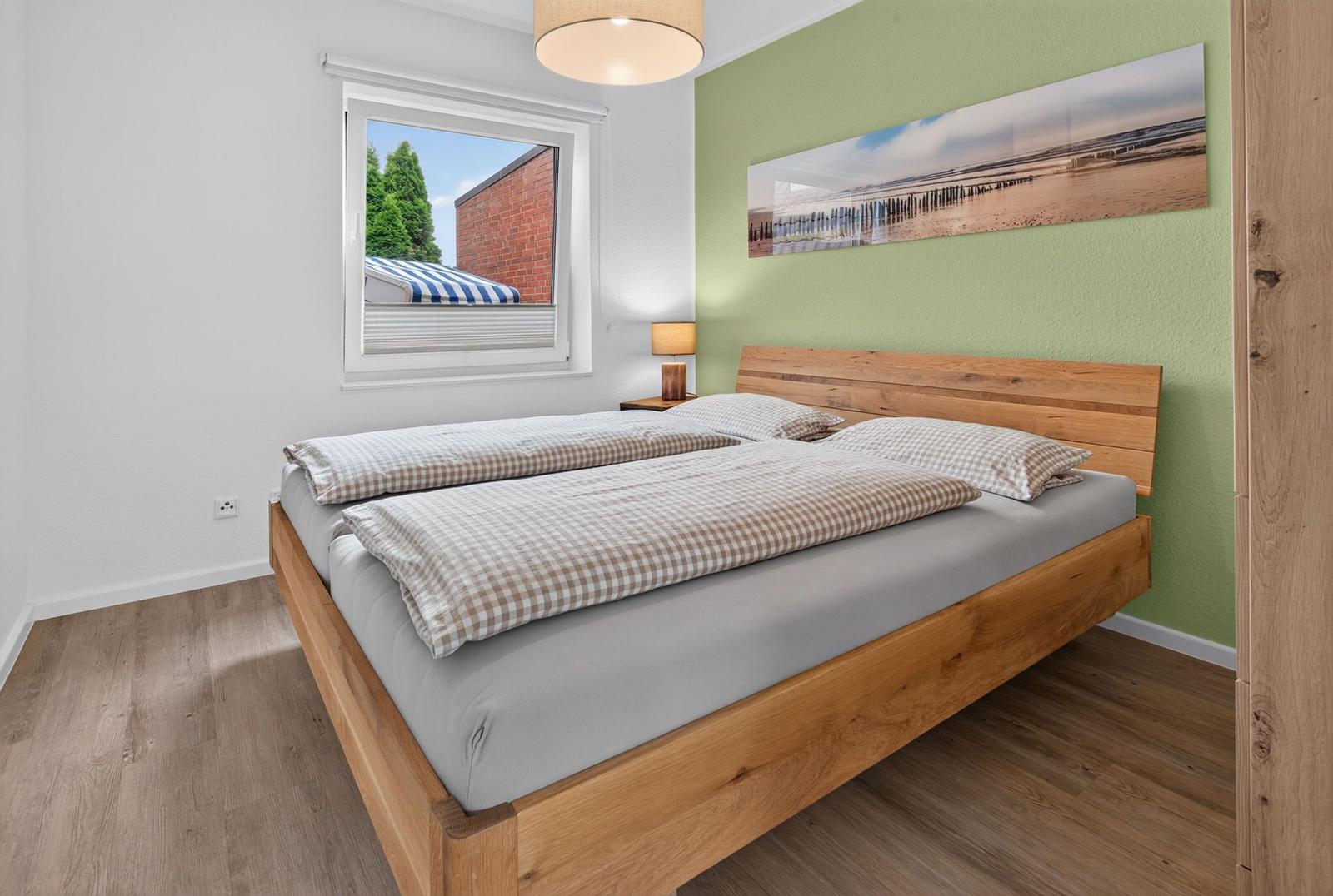 Schlafzimmer mit Holzbett, grüner Wand und Fensterblick auf Außenbereich.