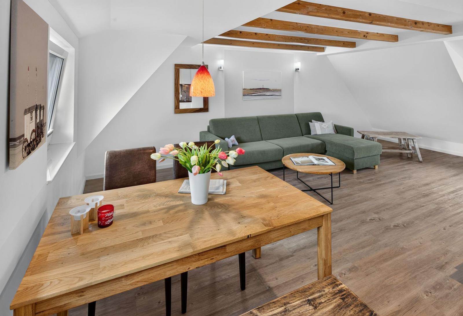 Wohn- und Essbereich mit grünem Sofa, Holztisch und Deckenbalken.
