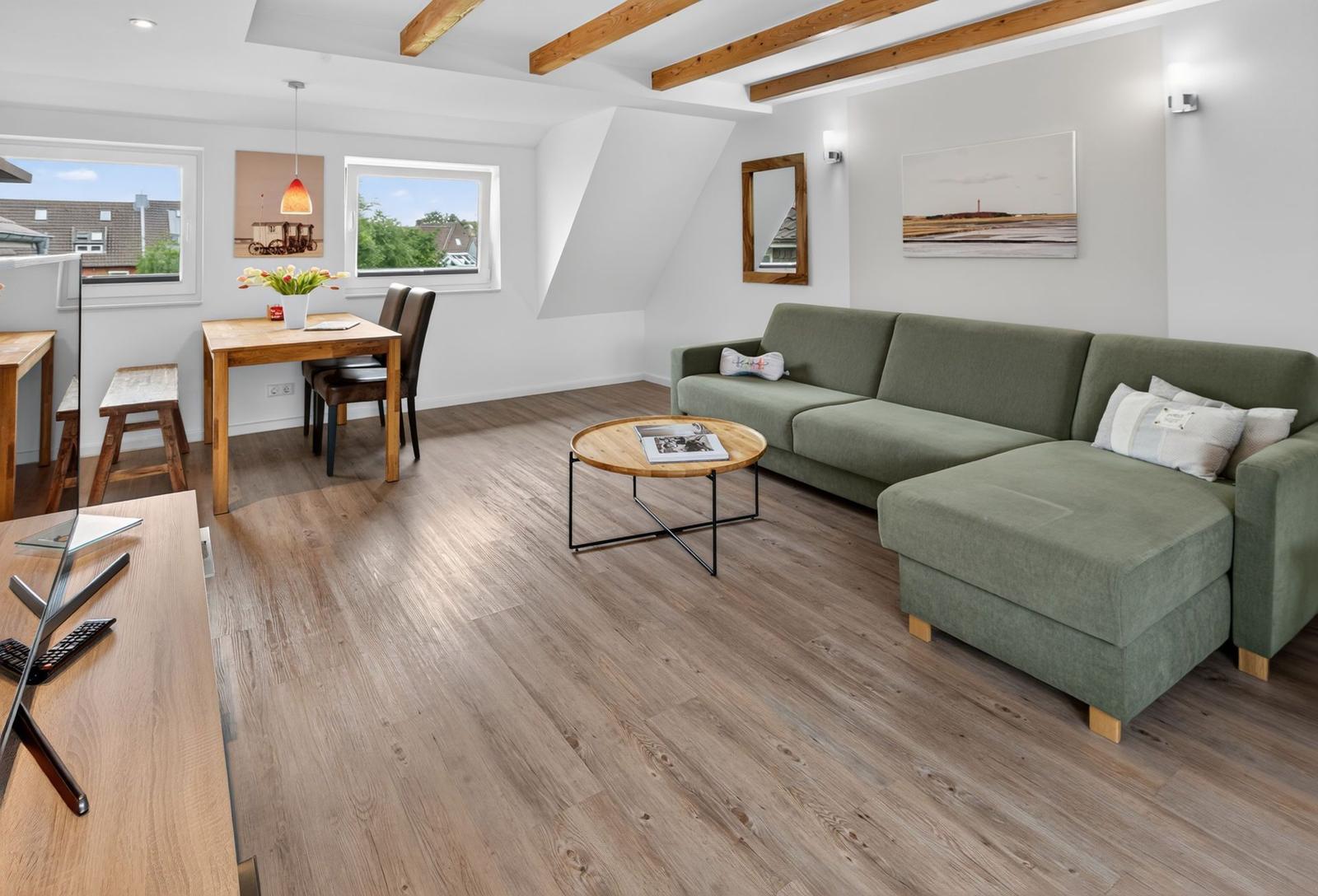 Wohn- und Essbereich mit grünem Sofa, Holzboden und Balkonfenstern.