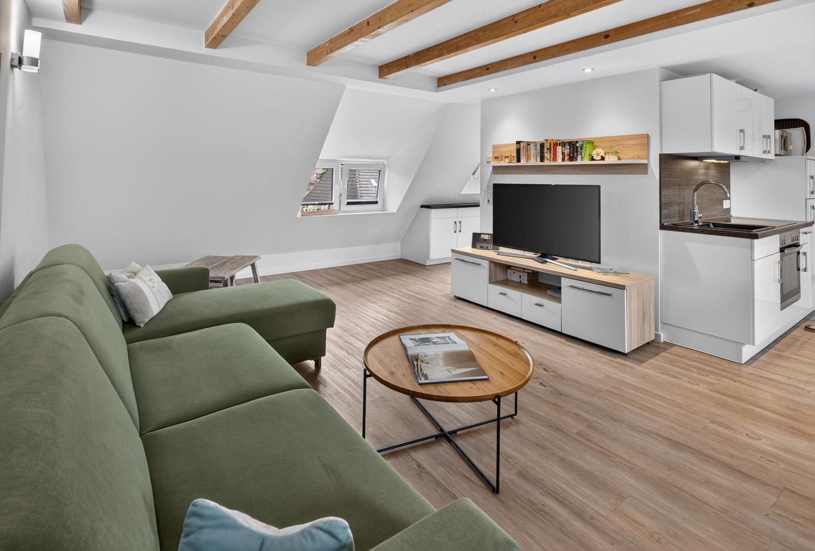 Wohnzimmer mit Sofa, TV und Küche unter Holzbalkendecke