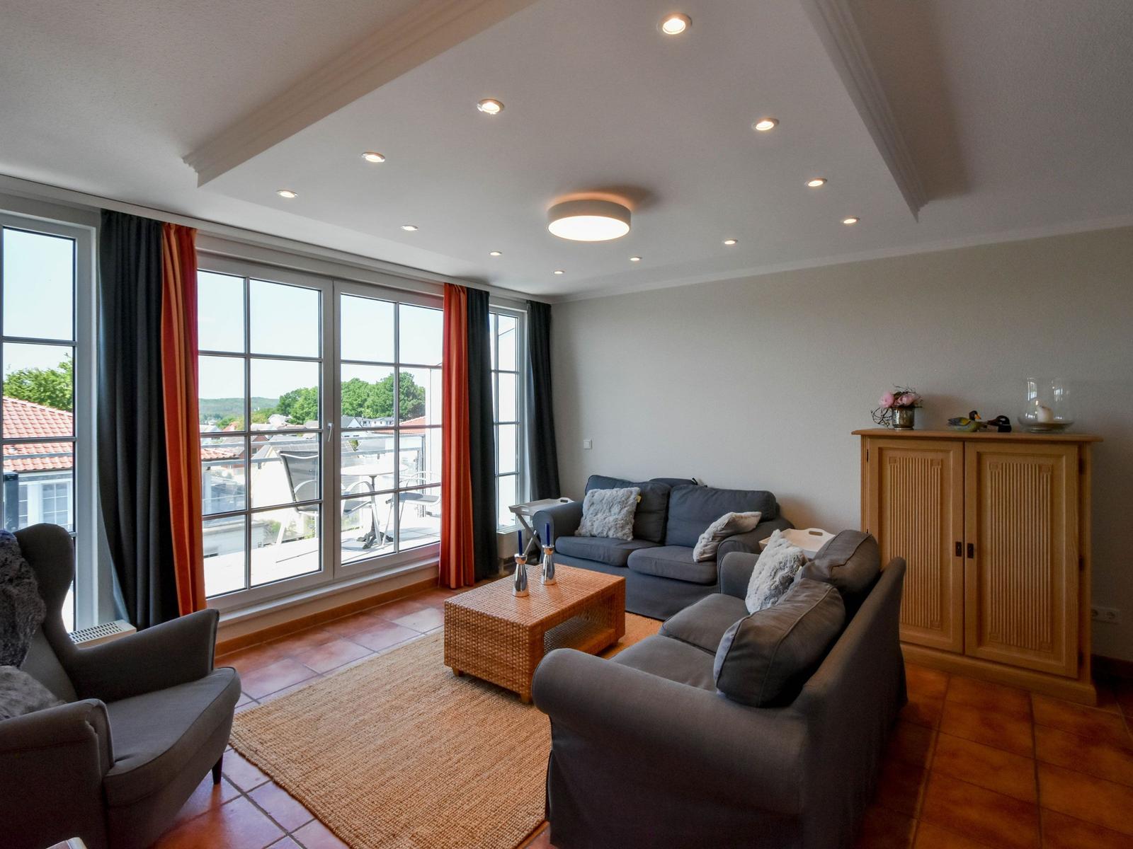 Wohnzimmer mit Sofa, Sessel und Terrasse. Holzfußboden und große Fenster.