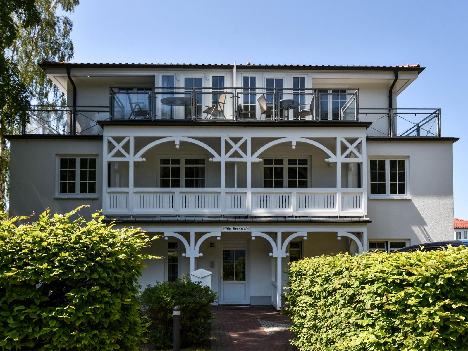 Villa Bernstein mit Balkon und Terrasse, umgeben von grünen Hecken.