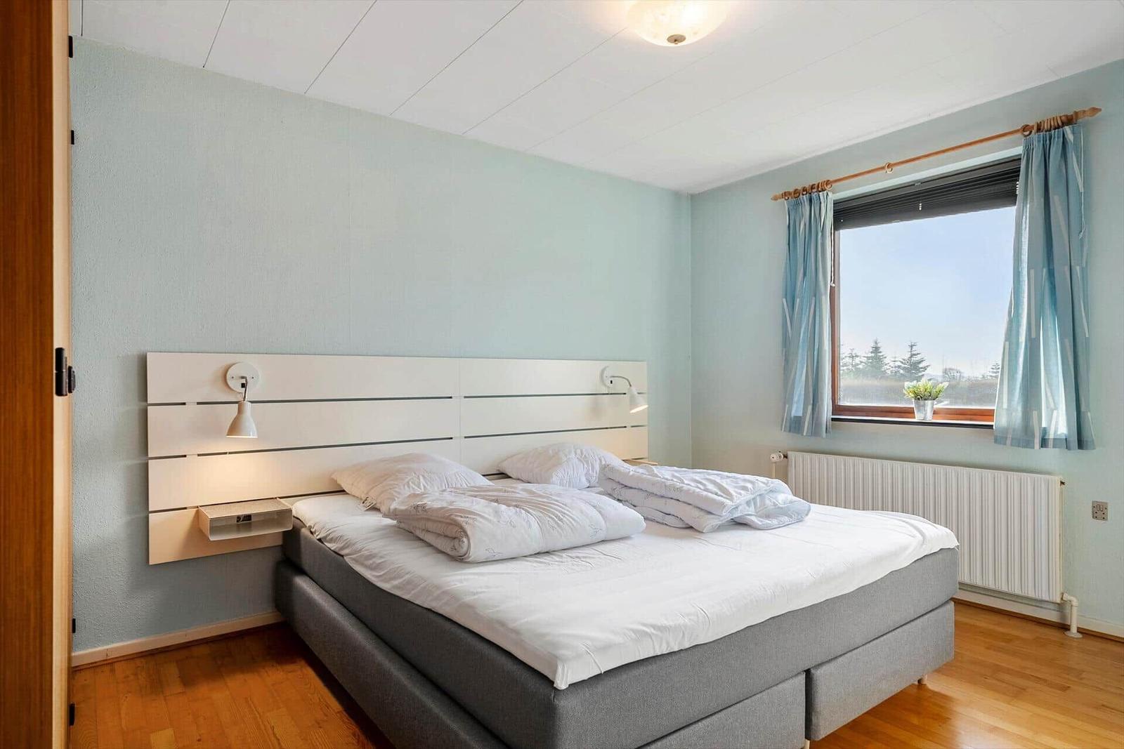Ein Schlafzimmer mit Doppelbett, Fenster mit Vorhängen und Stuhl.