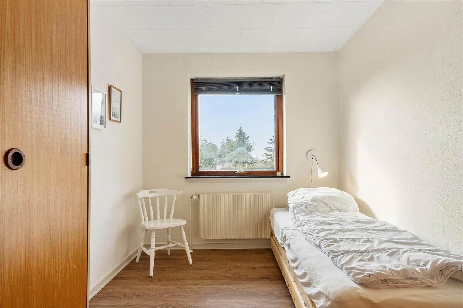Flur mit Holzschrank, Tür zu Schlafzimmer mit Fenster und Blick auf Bäume.