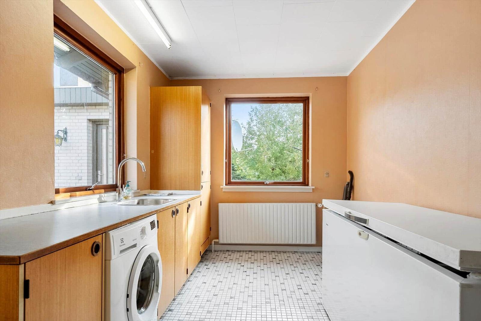 Bad mit Dusche, Waschbecken und Holzschränken. Fliesenwand und Fenster mit Pflanzen.