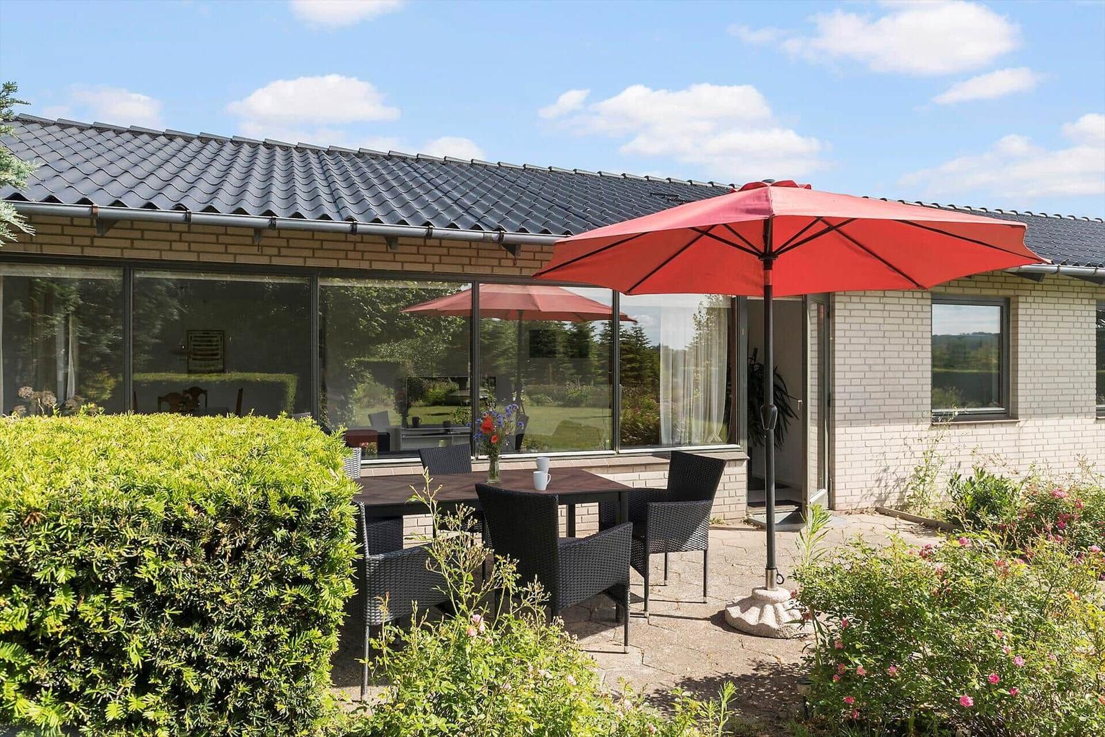 Ein modernes Haus mit Blumenbeet und Terrasse unter blauem Himmel.