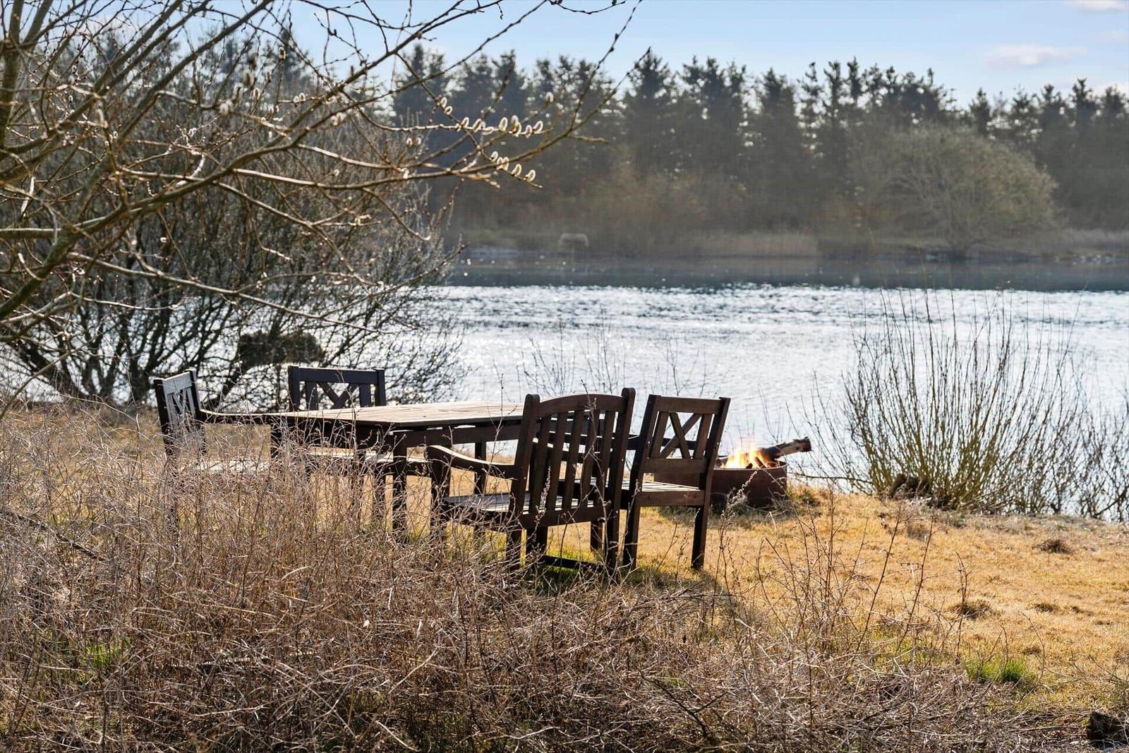 Außenbereich mit Feuerkorb und Holztisch mit Stühlen am See
