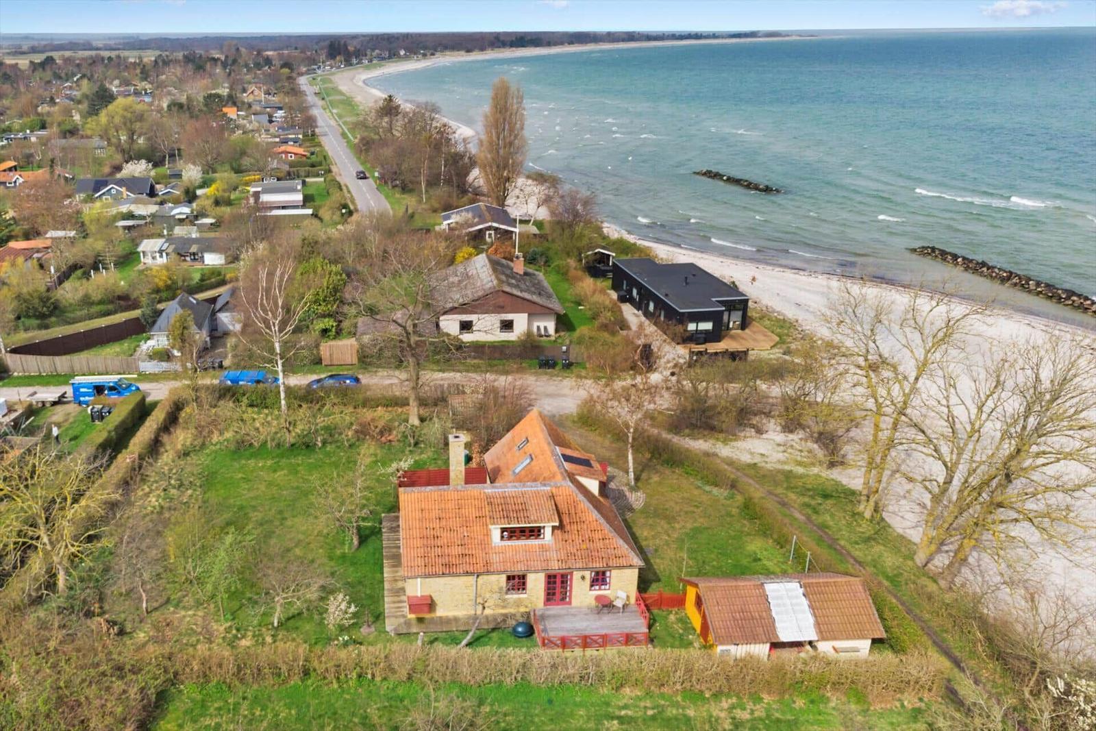 Haus mit Garten und Blick auf Strand. Mehrere Gebäude auf grünem Grundstück.