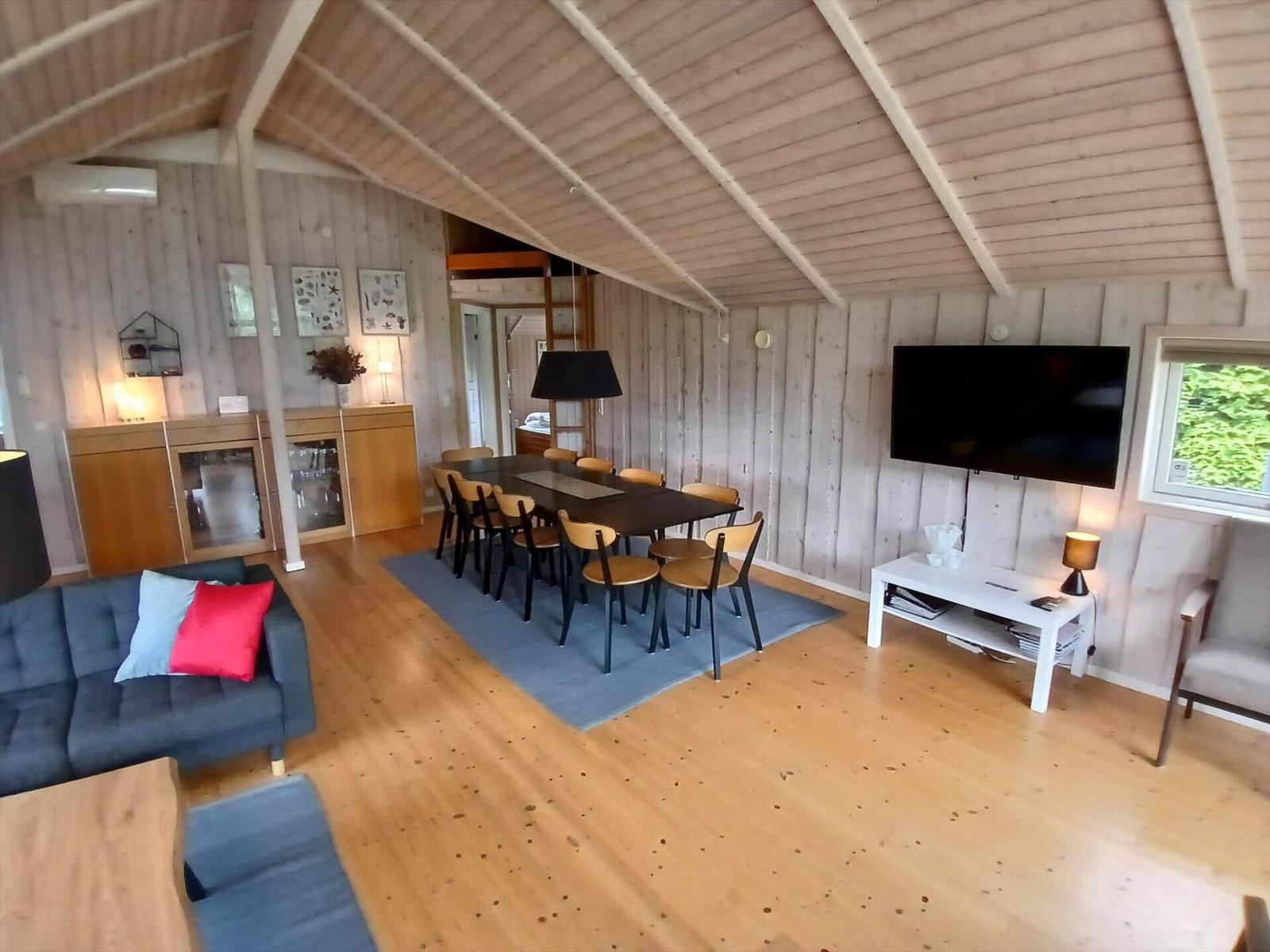 Rotes Holzhaus mit Terrasse und Garten. Außentisch mit Stühlen. Umgeben von Bäumen und Gras.