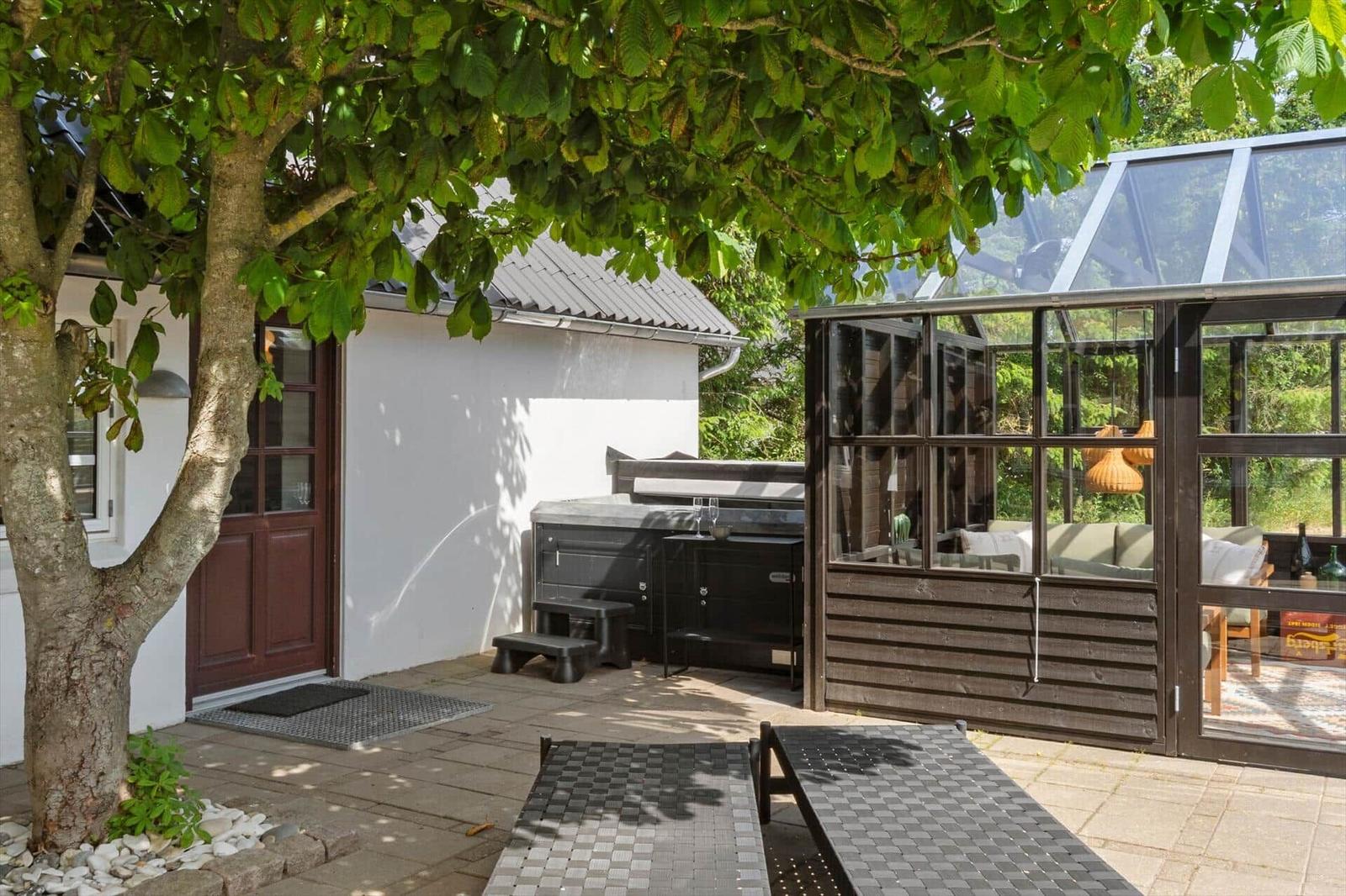 Terrasse mit Tischen, Stühlen und Sonnenschirm. Im Hintergrund Glasbau und Baum.